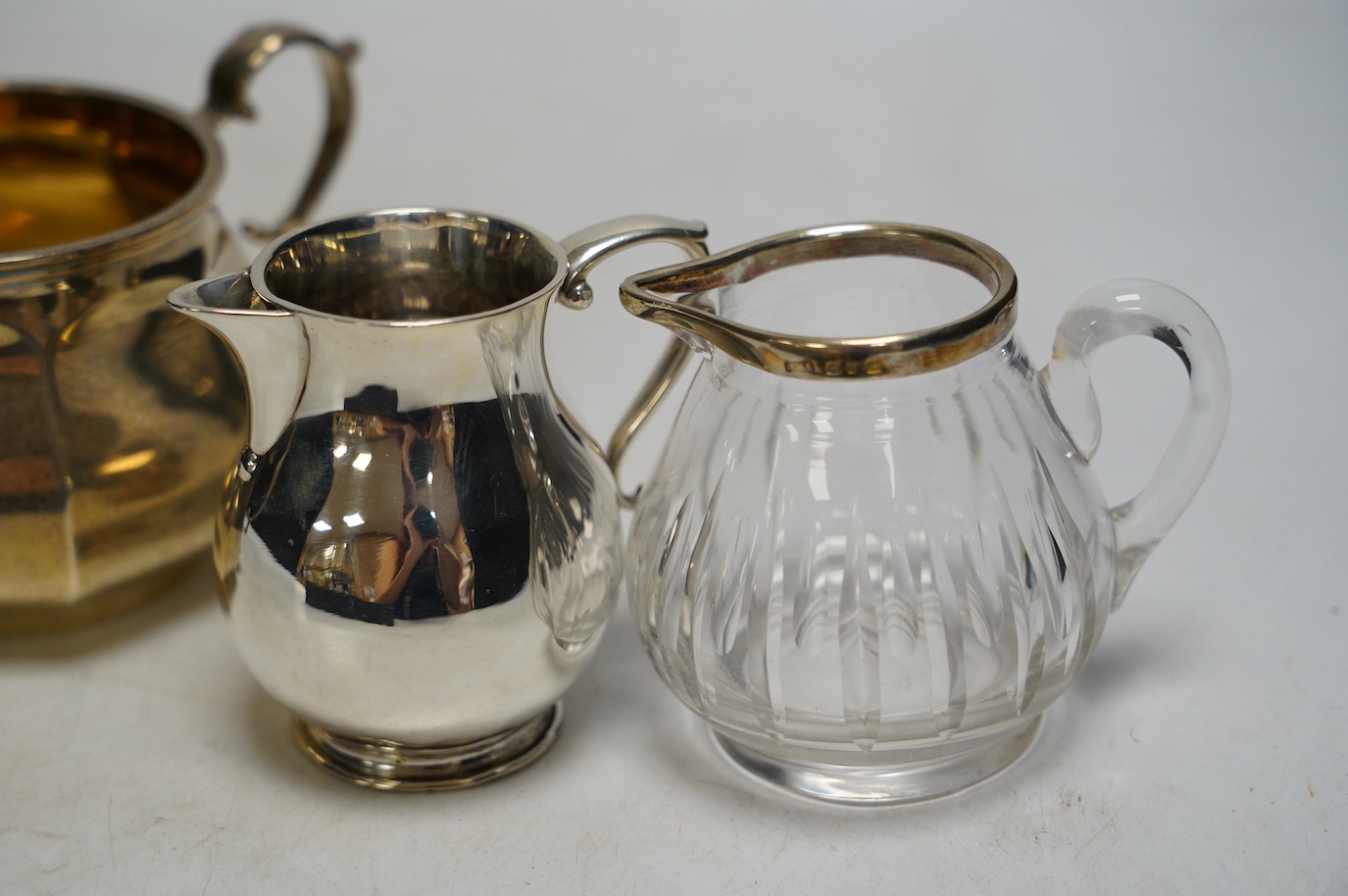 A George V silver two handled sugar bowl, Edward Barnard & Sons Ltd, London, 1926, two silver cream jugs including mounted glass and a white metal pepperette. Condition - poor to fair